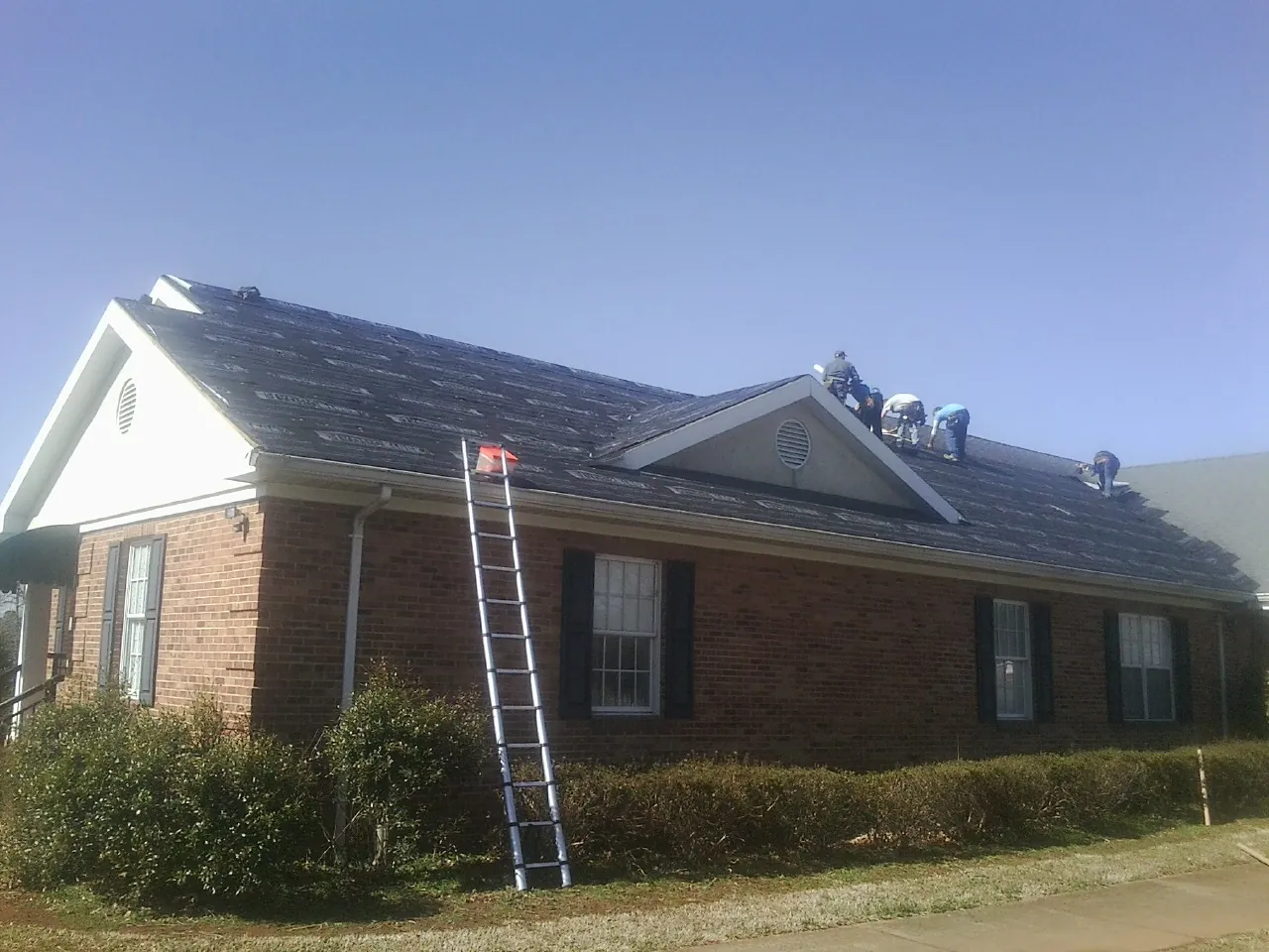 Crew tearing shingles off a brick ranch roof with a ladder set — Metal Roof Repair work by our crew in Ridgeville