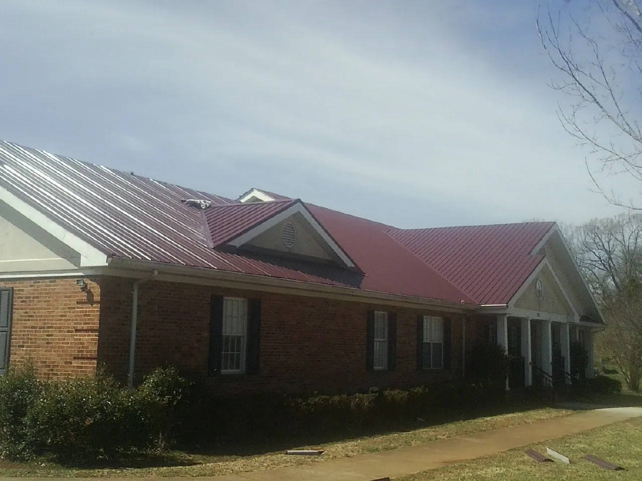 Red metal roof with gabled entries on a long brick building, from a Hail Damage Roof Repair job in Ridgeville