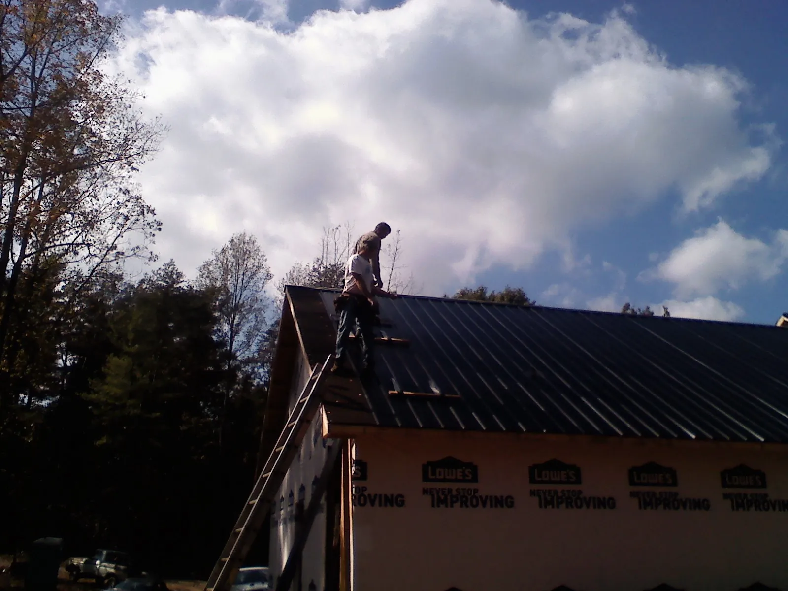Roofer fastening dark metal panels high against a cloudy sky, from a Roof Inspection job in Ridgeville